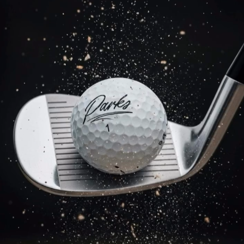 Wedge striking a Parks TRX golf ball with sand bursting around impact